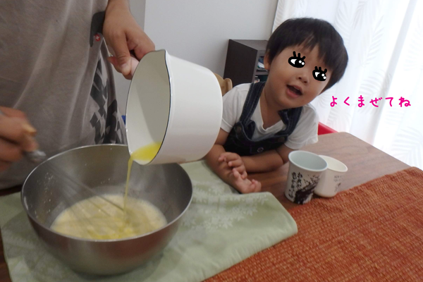 溶かしバターをクレープ生地に少しずつ加えて混ぜているのを見ている子供
